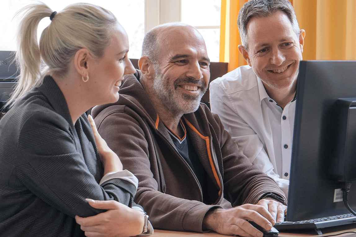 Ein Team von S&N Datentechnik, eine Mitarbeiterin und zwei Mitarbeiter vor einem Computerbildschirm